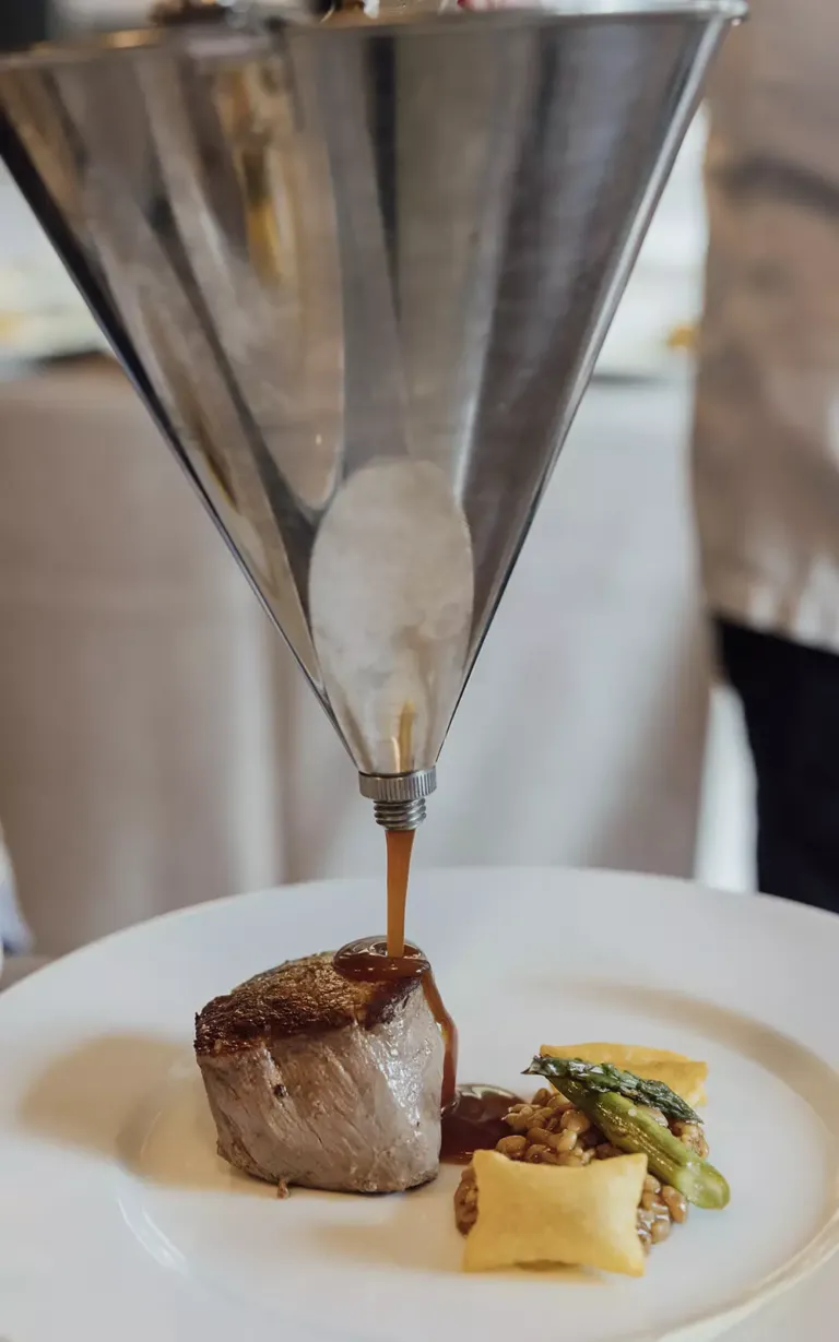 Primer plano de un embudo mientras se vierte salsa sobre carne