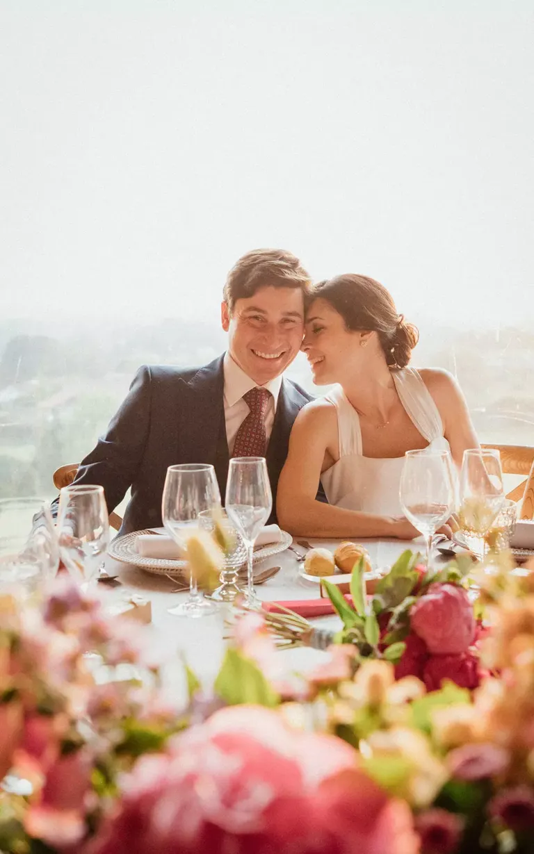Pareja de novios sonriendo sentados en la mesa